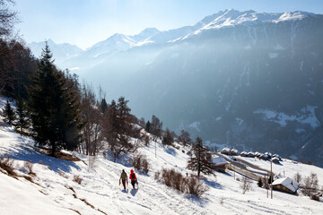 Fototapeta na wymiar Two people hiking in Valley of Herens, Switzerland, ski resort in winter