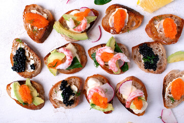 Assorted bruschetta with seafood, shrimp and caviar, avocado, cheese and radish on white table. Top view
