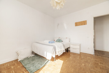 Fototapeta na wymiar Bedroom with double bed with chess parquet floor, white bedside table with drawers, green long hair rug and towels on the bed