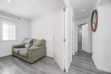 Living room with a small green sofa next to a window and a hallway with the same gray wooden floors
