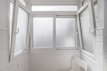 A small white tiled space with a chair of the same color and several aluminum windows