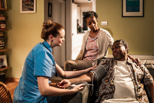 Young female caregiver checking the blood pressure of her senior patient at their home