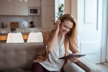 Young happy woman using a tablet on the couch at home