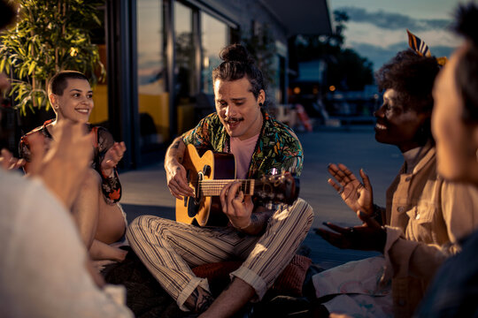 Young and diverse group of friends playing the guitar and singing along on vacation in their rented lake house