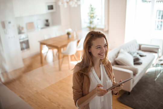 Young happy woman using her tablet in the living room at home - Powered by Adobe