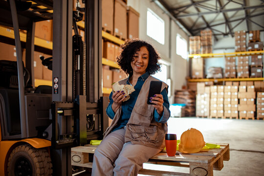 Young mixed woman using a smartphone while on a lunch break in warehouse