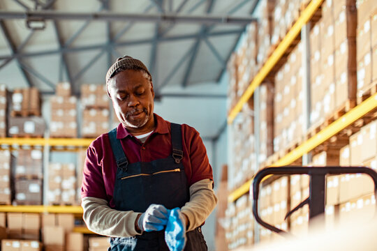 Mature African American man putting on his gloves while working in a warehouse