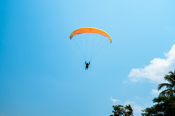 An adrenaline-pumping extreme sport, paragliding against the clear blue sky. Paraglider flying with his parachute above the sky with a background of blue sky and white clouds in a sunny day.