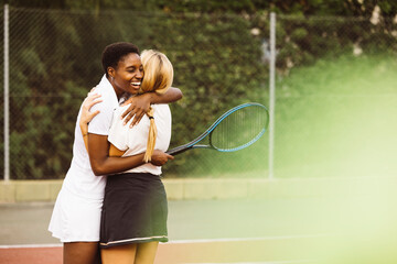 Portrait of two happy young beautiful women with tennis clothes and rackets in a tennis court ready to play a game. Two friends sharing a morning of sportive activity playing a tennis match. - obrazy, fototapety, plakaty