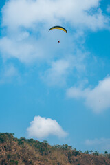 Paragliding attraction flying across hilly areas and clear blue skies. Paragliding is a sport that stimulates adrenaline by flying using a parachute in the wide sky