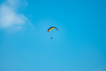 An adrenaline-pumping extreme sport, paragliding against the clear blue sky. Paraglider flying with his parachute above the sky with a background of blue sky and white clouds in a sunny day.