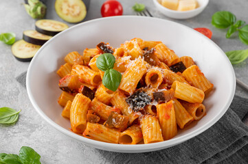 Pasta alla Norma. Italian pasta with eggplant, tomato sauce, cheese and basil in a gray concrete background. Comfort food.