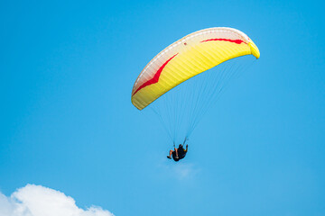 An adrenaline-pumping extreme sport, paragliding against the clear blue sky. Paraglider flying with his parachute above the sky with a background of blue sky and white clouds in a sunny day.
