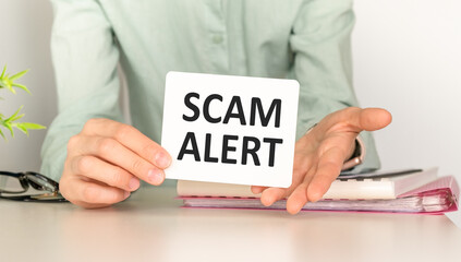 Closeup on business woman holding a card with Scam Alert message, business concept image with soft focus background