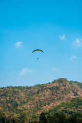Fototapeta na wymiar Paragliding attraction flying across hilly areas and clear blue skies. Paragliding is a sport that stimulates adrenaline by flying using a parachute in the wide sky