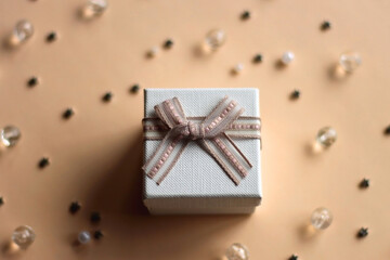 Small white present on neutral peachy background. Stars, pearls and beads in the background....
