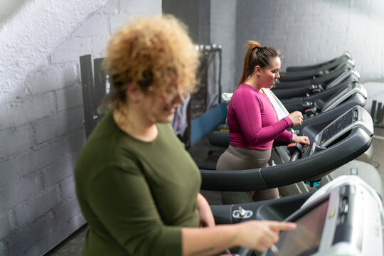 Two beautiful, overweight women power through a fitness routine, determined to achieve their goals. Workout on the treadmill.	