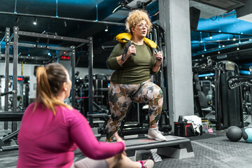 Two plus-size women embrace their bodies as they engage in a challenging workout. Doing squats at...