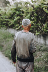 Naklejka na ściany i meble An old adult gray-haired thin homeless hungry man in dirty clothes walks along the street road in search of food. Photography, portrait.