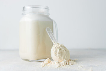 Glass jar of protein milkshake drink or smoothie and whey protein powder in measuring spoon on a...