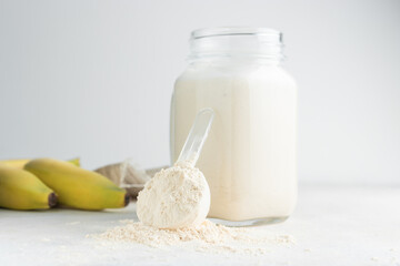 Glass jar of protein milkshake drink or smoothie and whey protein powder in measuring spoon, bananas on a white background. sport nutrition, bodybuilding food supplements