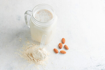 Glass jar of protein milkshake drink or smoothie and whey protein powder in measuring spoon, almond...