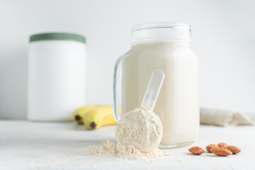 Whey protein powder in measuring spoon, glass jar of protein milkshake drink or smoothie, bananas and almond nuts on a white background. sport nutrition, bodybuilding food supplements