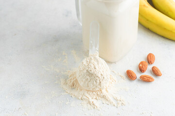 Whey protein powder in measuring spoon, glass jar of protein milkshake drink or smoothie, bananas and almond nuts on a white background. sport nutrition, bodybuilding food supplements