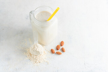 Glass jar of protein milkshake drink or smoothie and whey protein powder in measuring spoon, almond...