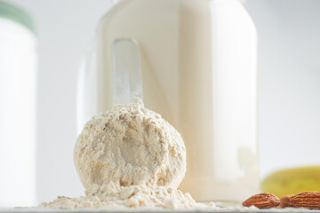 Whey protein powder in measuring spoon, glass jar of protein milkshake drink or smoothie, bananas and almond nuts on a white background. sport nutrition, bodybuilding food supplements