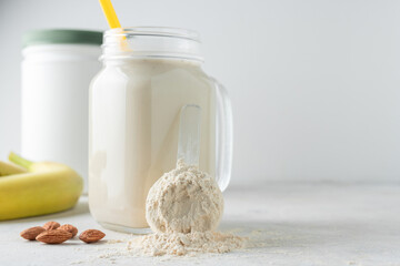 Whey protein powder in measuring spoon, glass jar of protein milkshake drink or smoothie, bananas and almond nuts on a white background. sport nutrition, bodybuilding food supplements