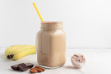 Glass jar of protein milkshake drink or smoothie and whey protein powder in measuring spoon,...