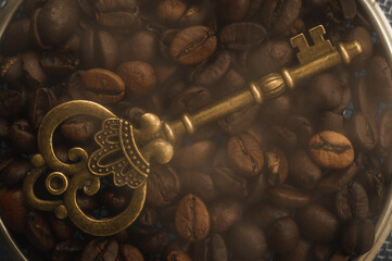 Golden vintage key on a background of hot coffee beans. An antique key against a background of coffee beans with smoke.