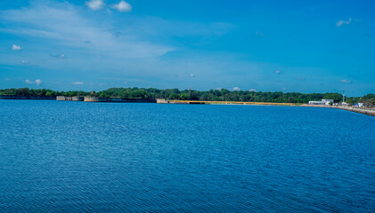 Blue sea with forest on the coast. Blue sky with white clouds.