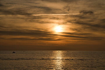 Sunset, illuminated sea. Sandy beach in the foreground. Light waves. Baltic Sea.