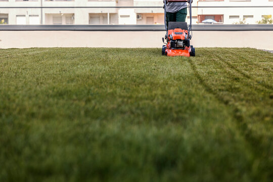 Cropped picture of a worker tidying up a lawn with a grass-cutting machine in a public space.