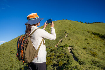 Girl on mountain peak with green grass and use of mobile phone to take photo on mountain valley