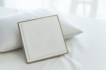 mockup of white frame on a soft bed leaning against white pillow, blurred background for mockup applications.