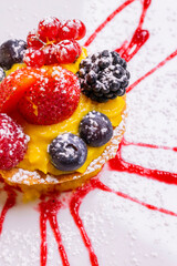 Crostata di frutta con crema pasticcera guarnita con topino alla fragola e zucchero a velo servita come dolce in un ristorante elegante