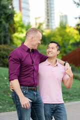 Smiling attractive homosexual couple embracing looking at each other standing on urban street