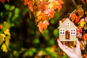 The symbol of the house in the girl's hand on the background of red leaves
