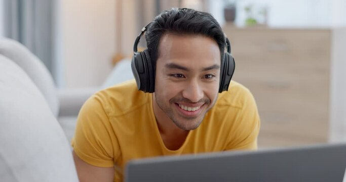Headphones, laptop and young man on a sofa watching a funny, comic or comedy movie in the living room. Happy, laugh and Indian male person streaming a film or show on computer in the lounge at home.