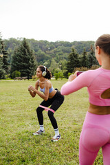 Woman making video with smartphone camera of her friend squatting with resistance band in park