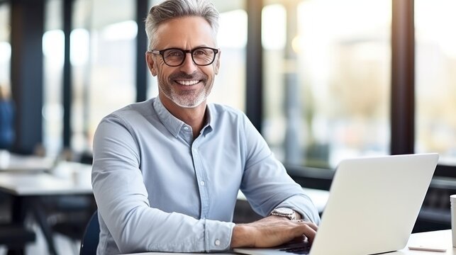 Smiling mature businessman in eyeglasses working on laptop in office