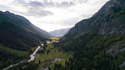 Fototapeta na wymiar Beautiful sunset with a view of the green gorge and the river. coniferous trees, forests, lots of grass are all around. A seething gray river. Clouds in the sky. The rays of the sun. Steep cliffs