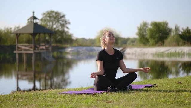 A woman sits in the lotus position meditating by a lake