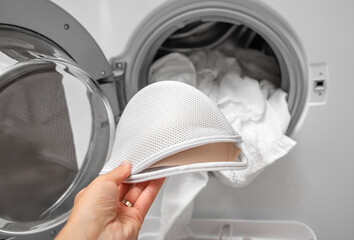 A hand puts women's underwear into the washing machine. Close-up.
