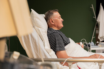 Hospitalized senior with oxygen tube, fingertip monitor, fatigue evident likely recovering from a...