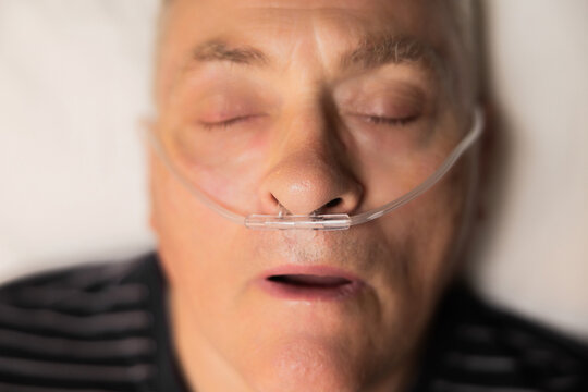 Sleeping senior man with an oxygen tube in his nose and his mouth gently open in hospital