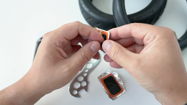 Close-up of a repairman holds a rubber patch in his hands to seal a hole in a wheel inner tube. Replacement of a rubber tire for an electric scooter wheel. Wheels disassembly and repairs in workshop